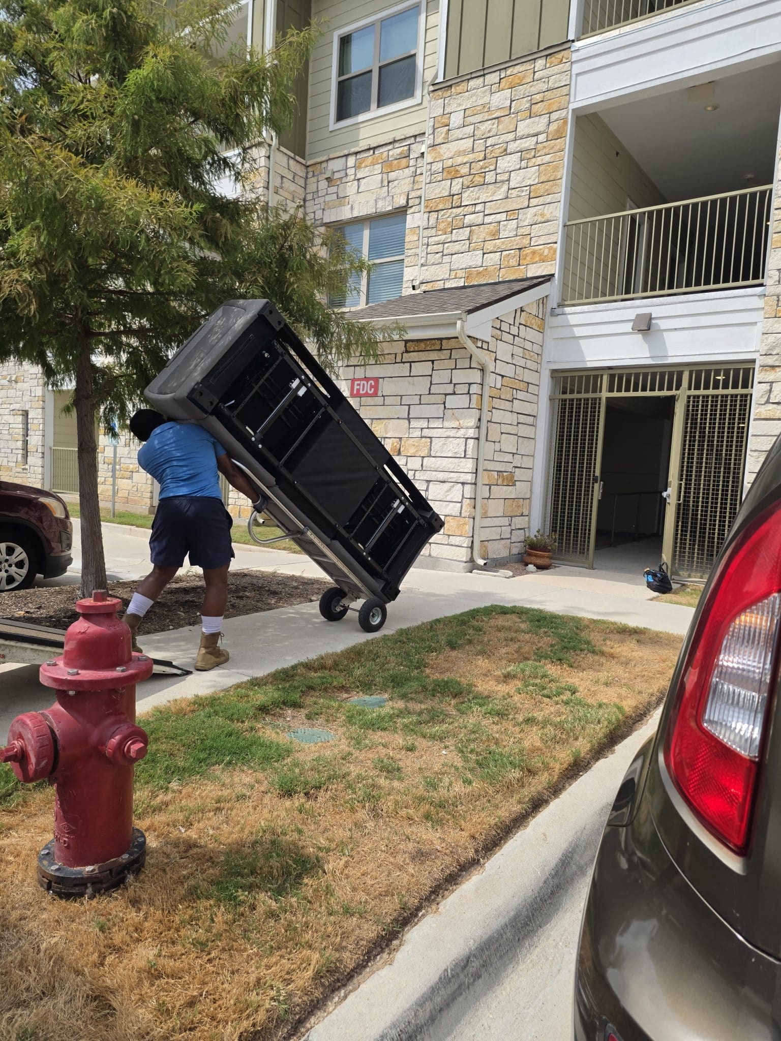 Moto Movers crew dollying large furniture item Moto Movers moving a large couch on a dolly outside Legacy Senior Apartments, apartment building in Round Rock, Texas.