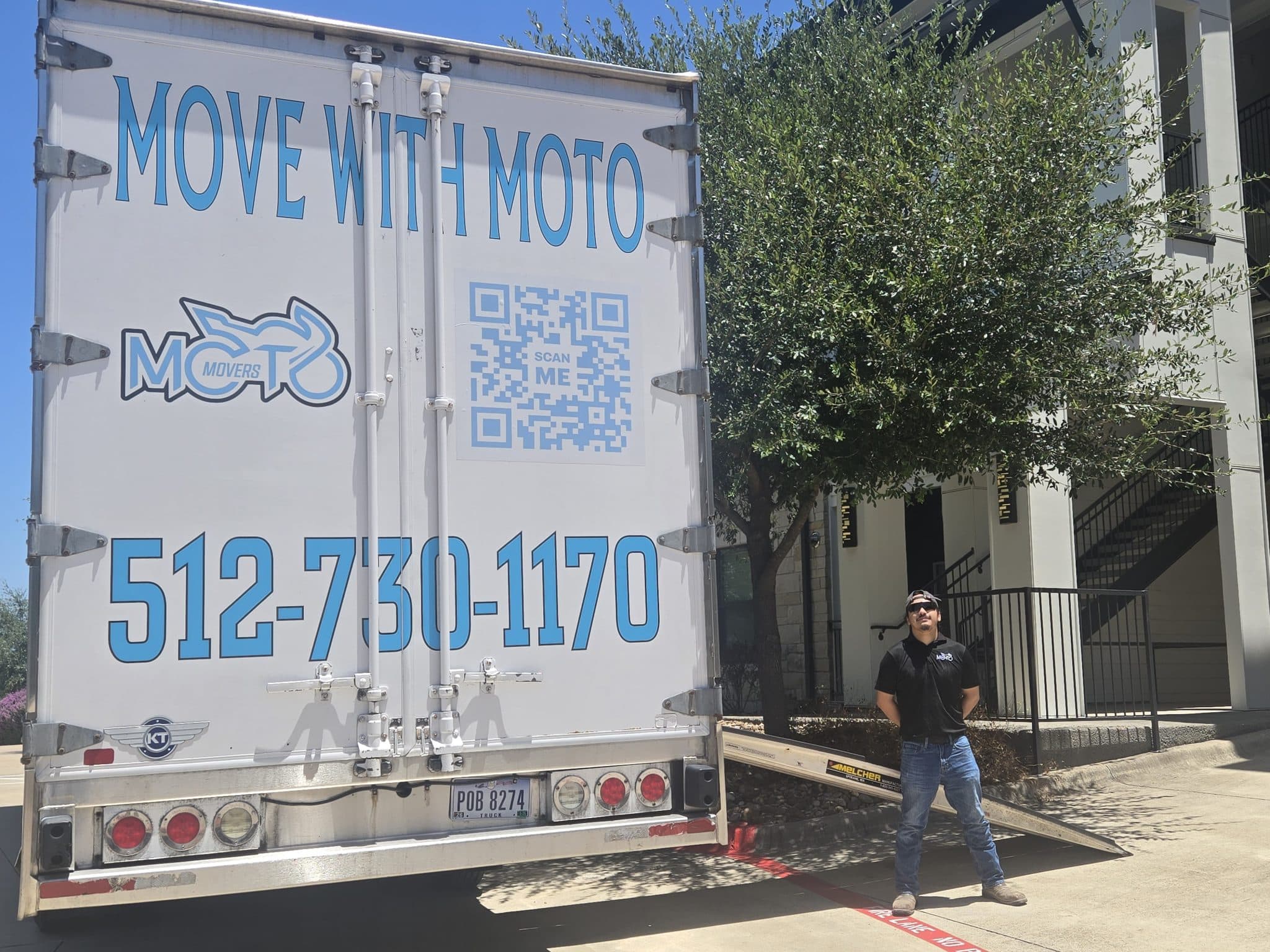 Moving truck with Moto logo and contact info, parked by a building; a man stands near the truck.